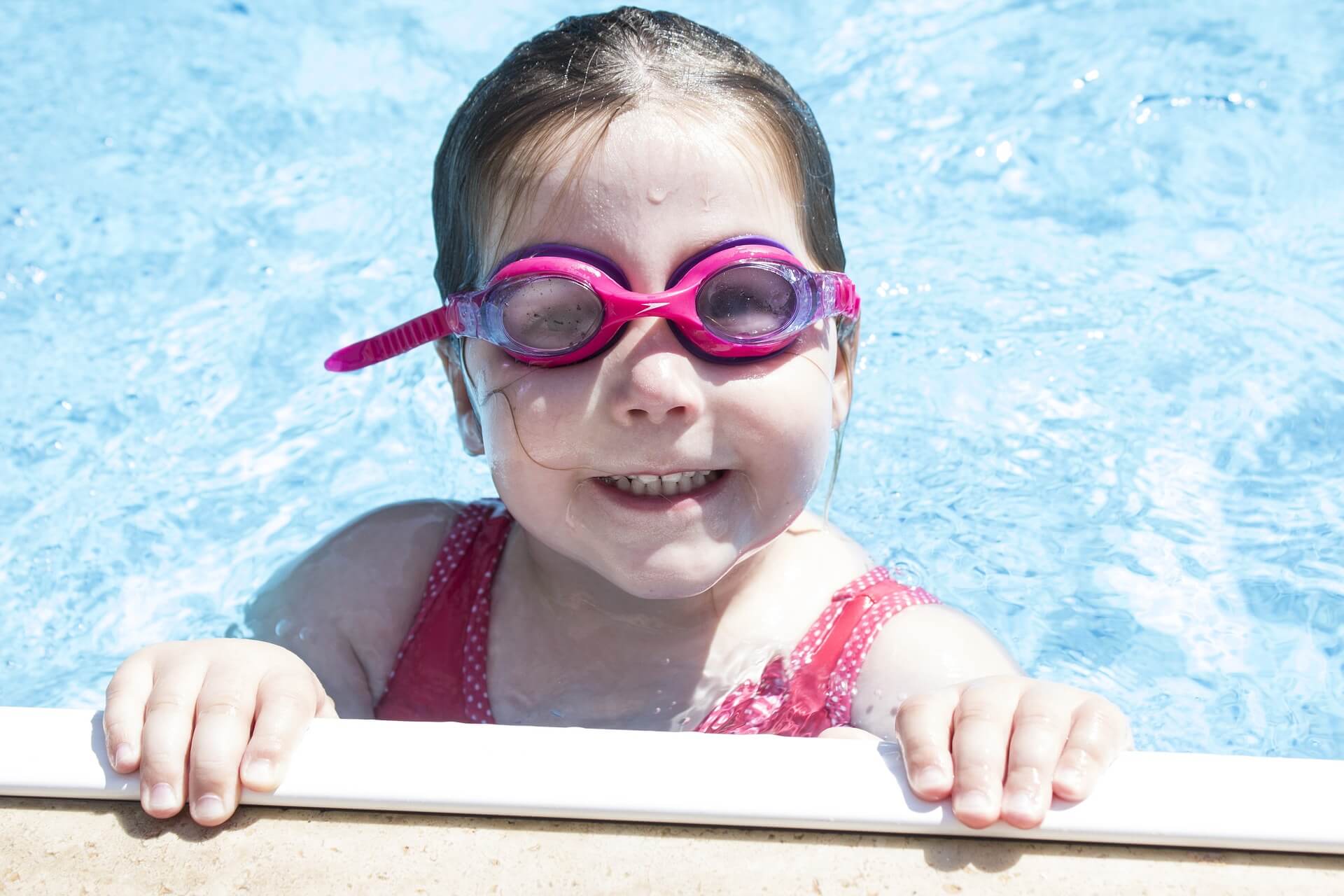 Ein Mdchen mit einer pinken Schwimmbrille hält sich am Poolrand fest