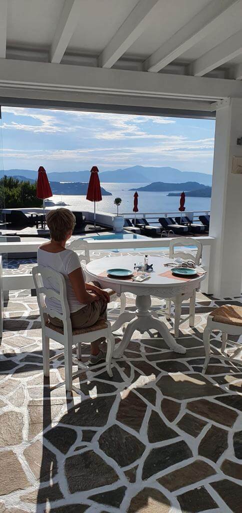 Jeannette sitzt in einer griechischen Taverne und genießt den Ausblick von der Terrasse auf eine Bucht