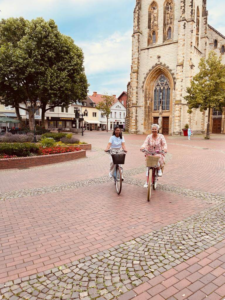 Zwei Frauen auf einem Fahrrad vor einer Kirche auf Pflastersteinen