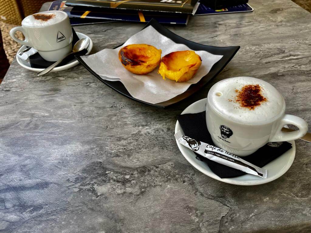 Zwei Kaffetassen mit viel Schaum und Kakao und dazu die berühmten portugiesischen Köstlichkeiten Pastel de Nata