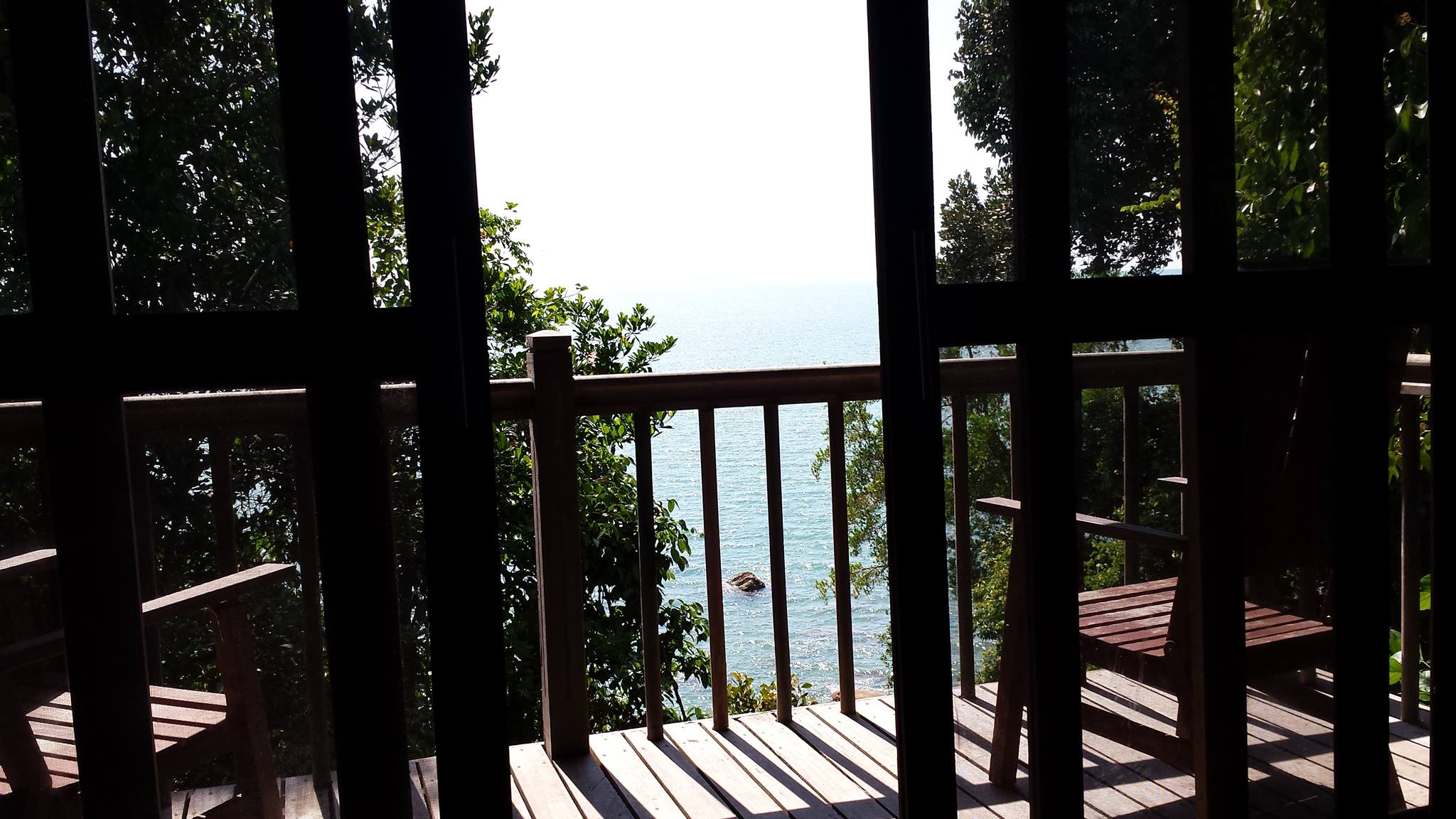 Ein Blick von einer holzverkleideten Terrasse einer vietnamesischen Unterkunft auf eine schmale von Bäumen umsäumte Bucht