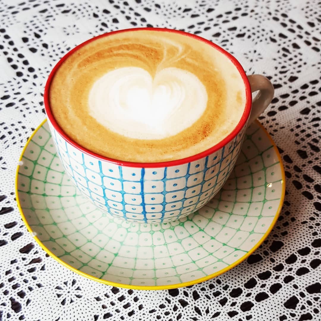 Eine nostalgische Kaffeetasse mit Untertasse auf einer Lochspitzentischdecke, der Schaun hat ein Herzmuster