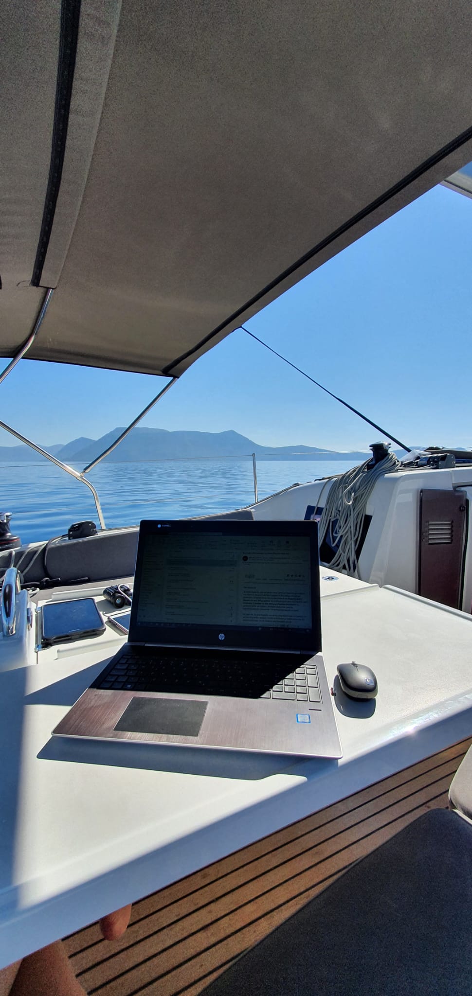 Ein offenes Notebook auf einem schattigen Plätchen auf einem Boot mit Meerblick